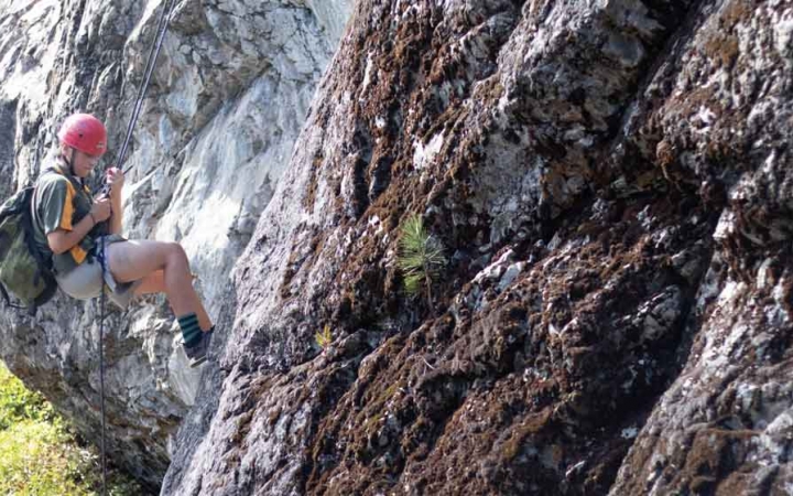a student pauses to look down while rock climbing on an outward bound trip